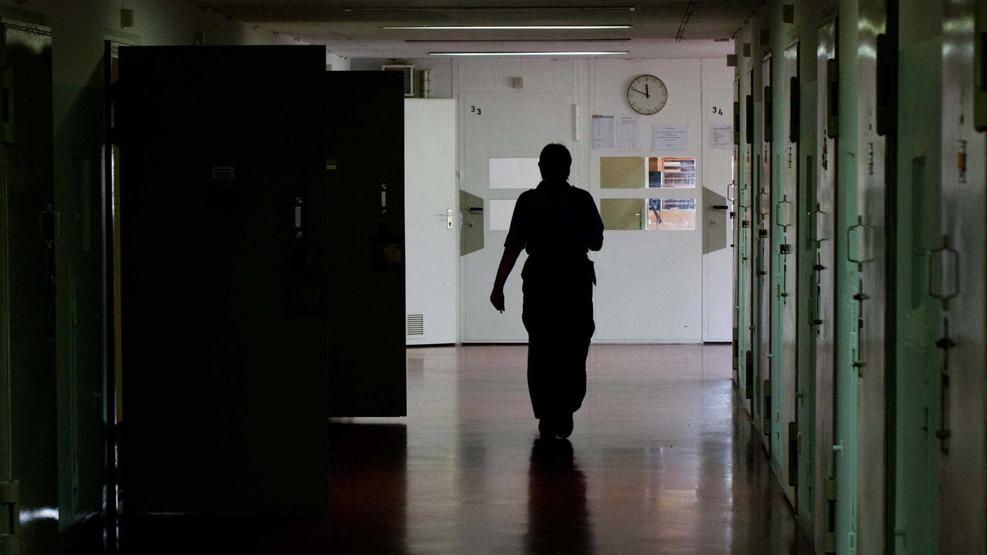 Ein Justizbeamter geht durch einen dunklen Flur einer Justizvollzugsanstalt.