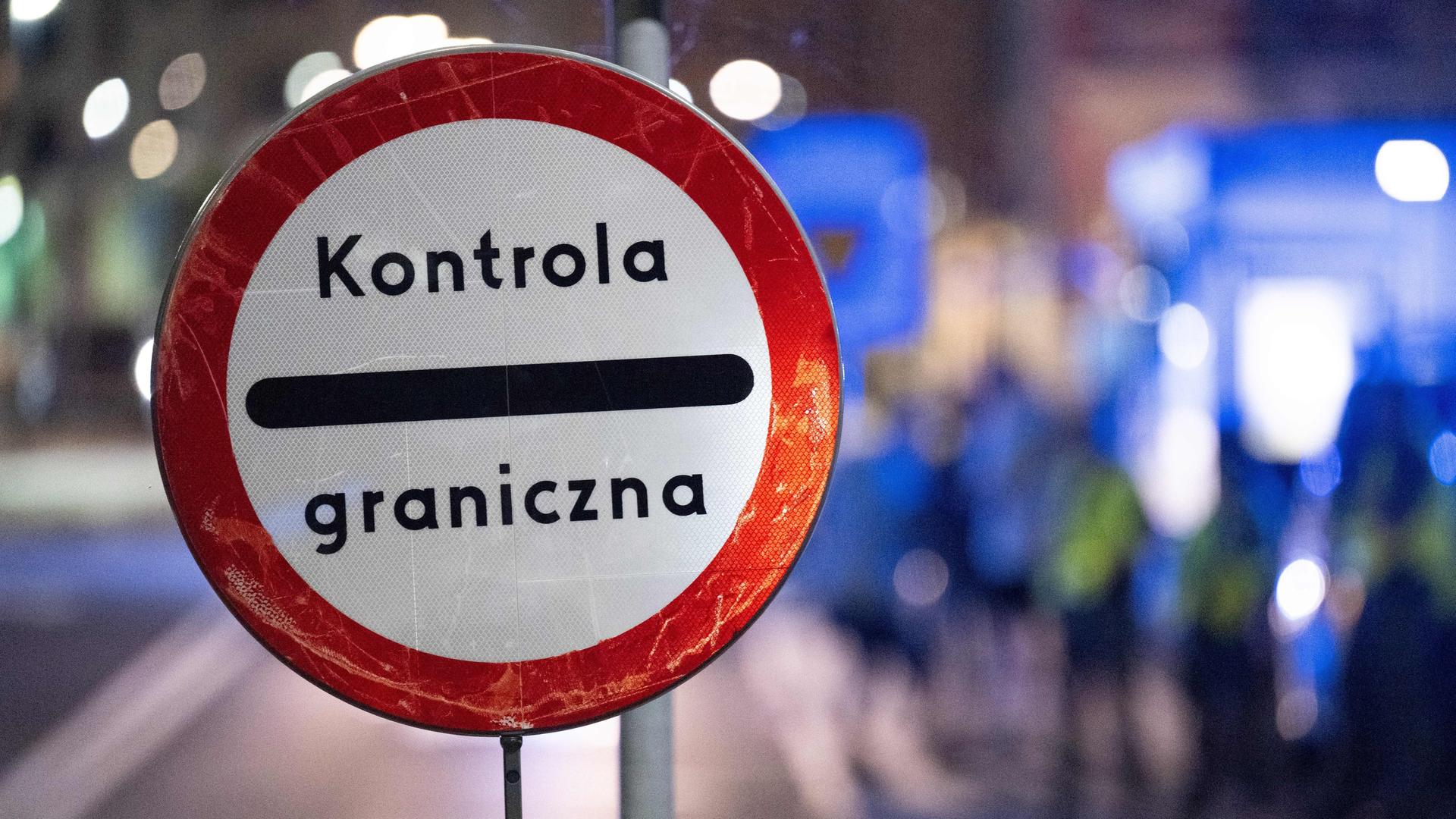 Auf einem runden Schild steht "Kontrola graniczna", polnisch für Grenzkontrolle. Im Hintergrund sind unscharf polnische Grenzschützer zu sehen. Auf einem runden Schild steht "Kontrola graniczna", polnisch für Grenzkontrolle. Im Hintergrund sind unscharf polnische Grenzschützer zu sehen.