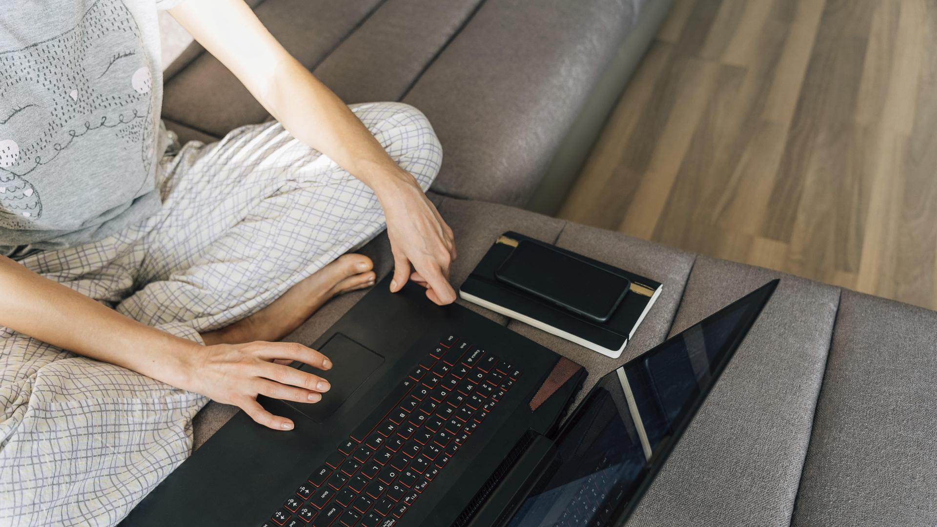 Eine Frau in Hauskleidung mit einem Laptop, neben ihr ein Notizbuch und ein Stift.