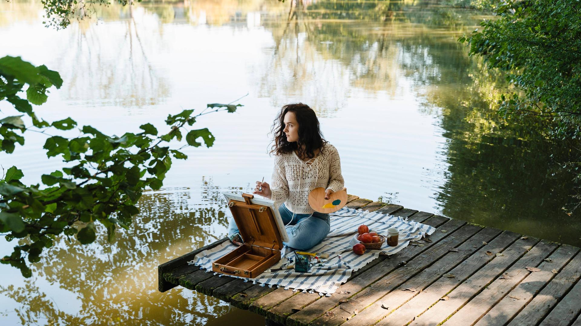 Eine Frau sitzt an einem See und malt