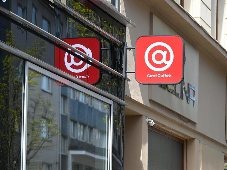 Schild der Kaffeekette Cotti Coffee an einer Hausfassade - ein weißes @-Zeichen auf rotem Grund Schild der Kaffeekette Cotti Coffee an einer Hausfassade - ein weißes @-Zeichen auf rotem Grund