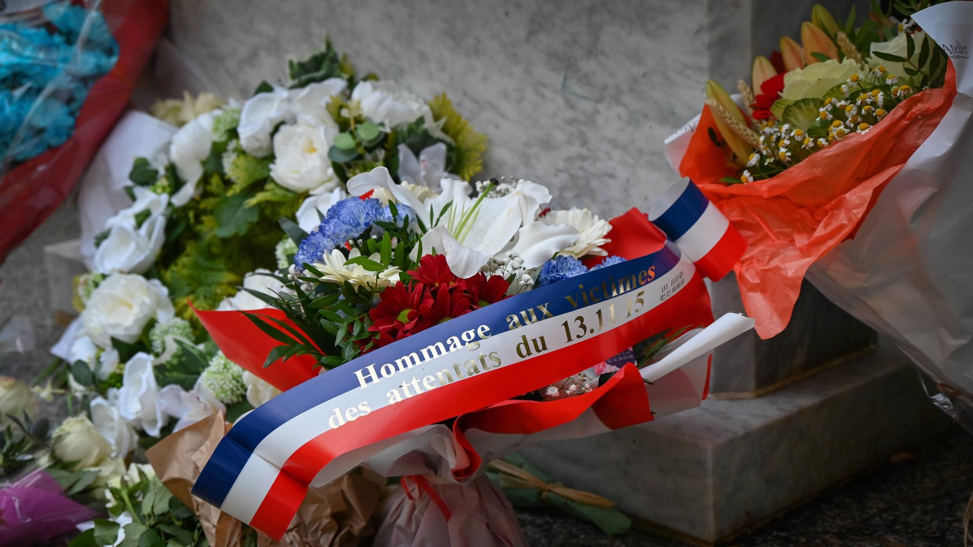 Ein Blumengesteck mit einer Schleife in den Farben der französischen Nationalflagge, auf dem steht: "Hommage an die Opfer der Anschläge vom 13. November 2015".