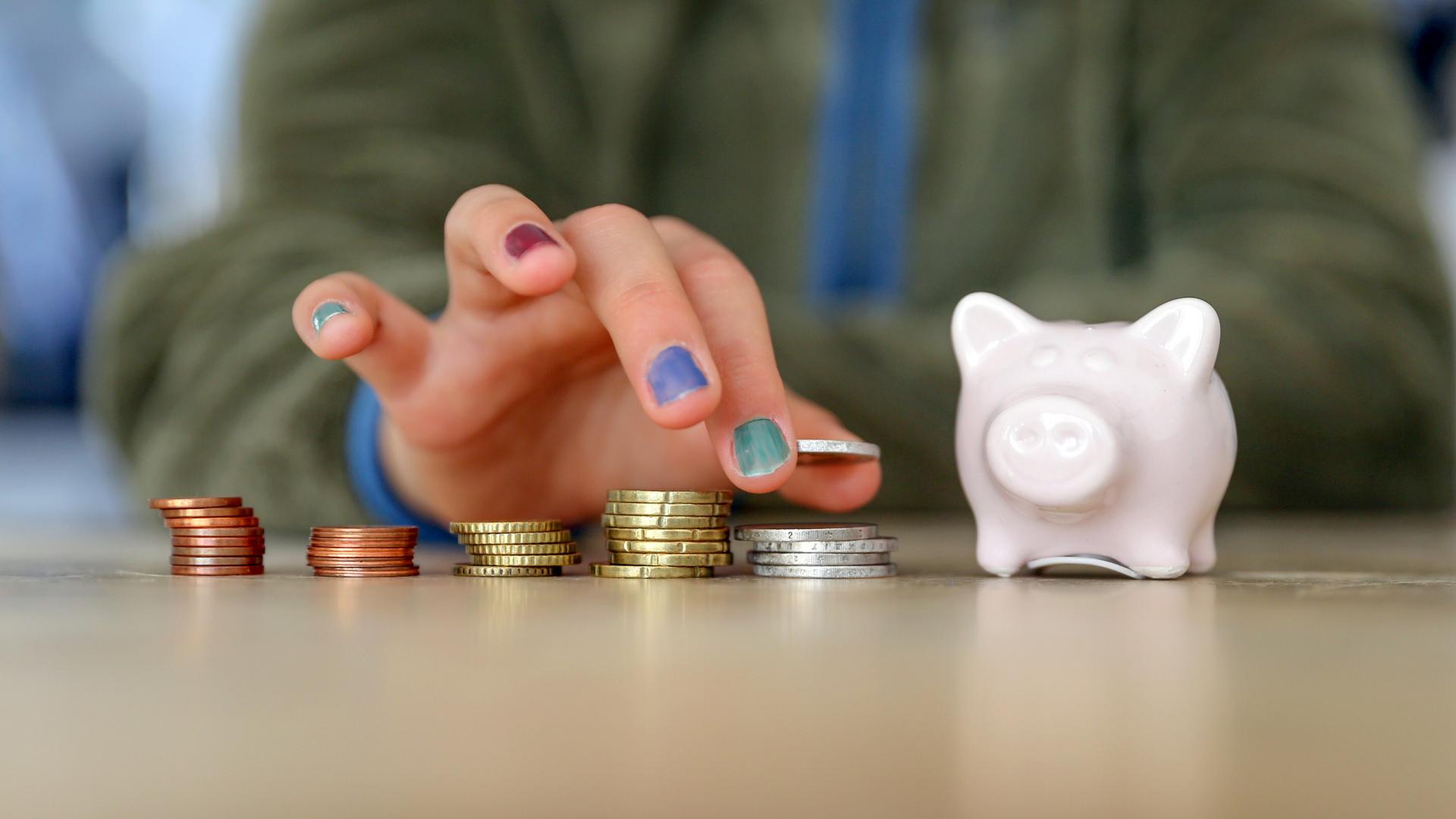 Hand mit lackierten Fingernägeln stapelt Geldmünzen neben einem Sparschwein Hand mit lackierten Fingernägeln stapelt Geldmünzen neben einem Sparschwein
