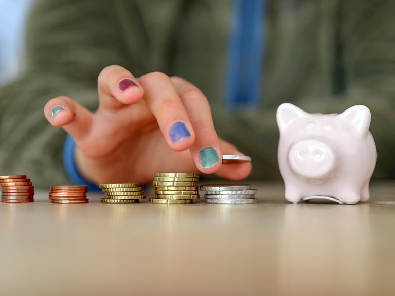 Hand mit lackierten Fingernägeln stapelt Geldmünzen neben einem Sparschwein