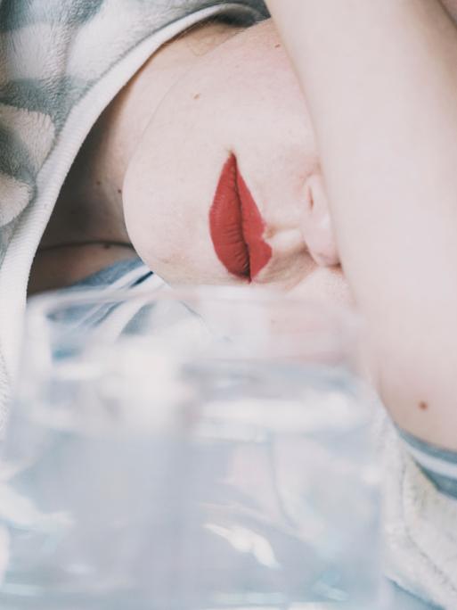 Eine junge Frau verdeckt ihre Augen mit ihrem Arm, vor ihr ein Glas Eine junge Frau verdeckt ihre Augen mit ihrem Arm, vor ihr ein Glas