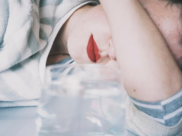 Eine junge Frau verdeckt ihre Augen mit ihrem Arm, vor ihr ein Glas Eine junge Frau verdeckt ihre Augen mit ihrem Arm, vor ihr ein Glas