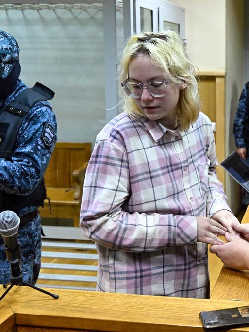 Diana Loginowa vor Gericht in St. Petersburg, neben ihr steht ein vermummter russischer Polizist  (11.11.2025)