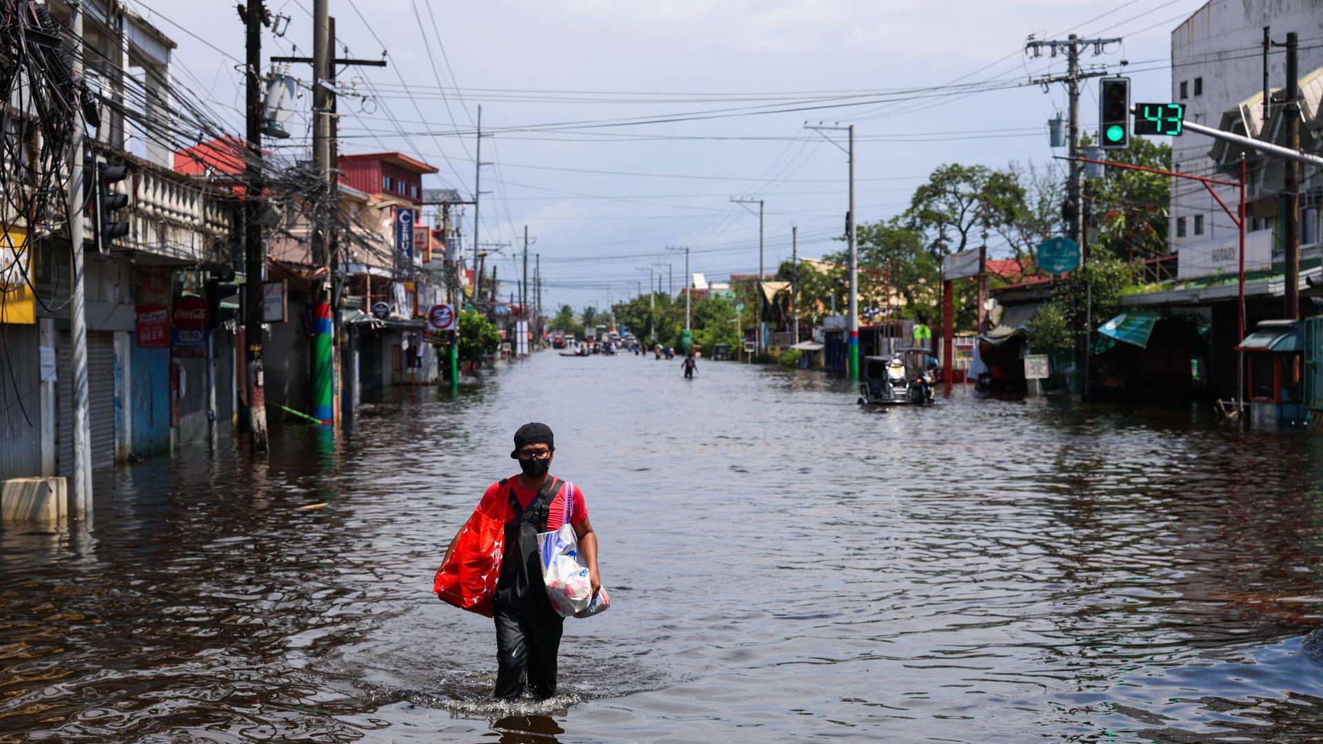 In Pampanga, in den Philippinen, geht ein Mann über eine Straße, die unter Wasser steht. Er trägt zwei Taschen bei sich. In Pampanga, in den Philippinen, geht ein Mann über eine Straße, die unter Wasser steht. Er trägt zwei Taschen bei sich.