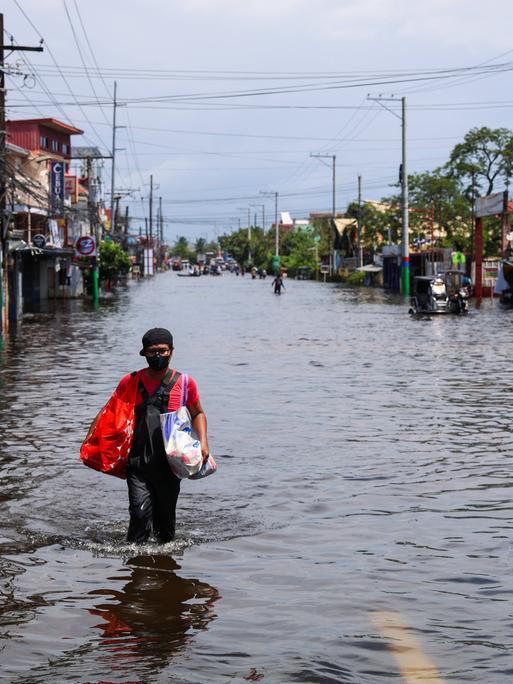 In Pampanga, in den Philippinen, geht ein Mann über eine Straße, die unter Wasser steht. Er trägt zwei Taschen bei sich. In Pampanga, in den Philippinen, geht ein Mann über eine Straße, die unter Wasser steht. Er trägt zwei Taschen bei sich.