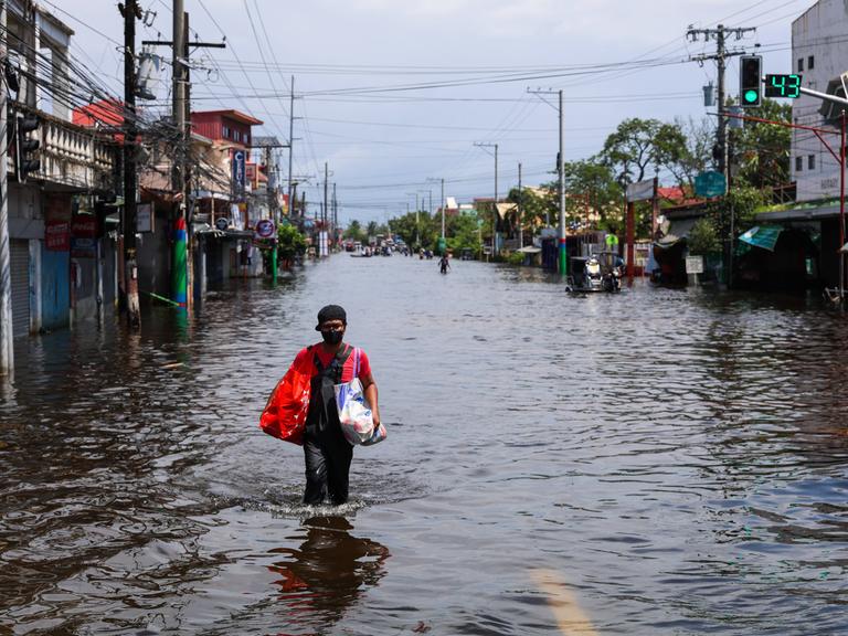 In Pampanga, in den Philippinen, geht ein Mann über eine Straße, die unter Wasser steht. Er trägt zwei Taschen bei sich. In Pampanga, in den Philippinen, geht ein Mann über eine Straße, die unter Wasser steht. Er trägt zwei Taschen bei sich.
