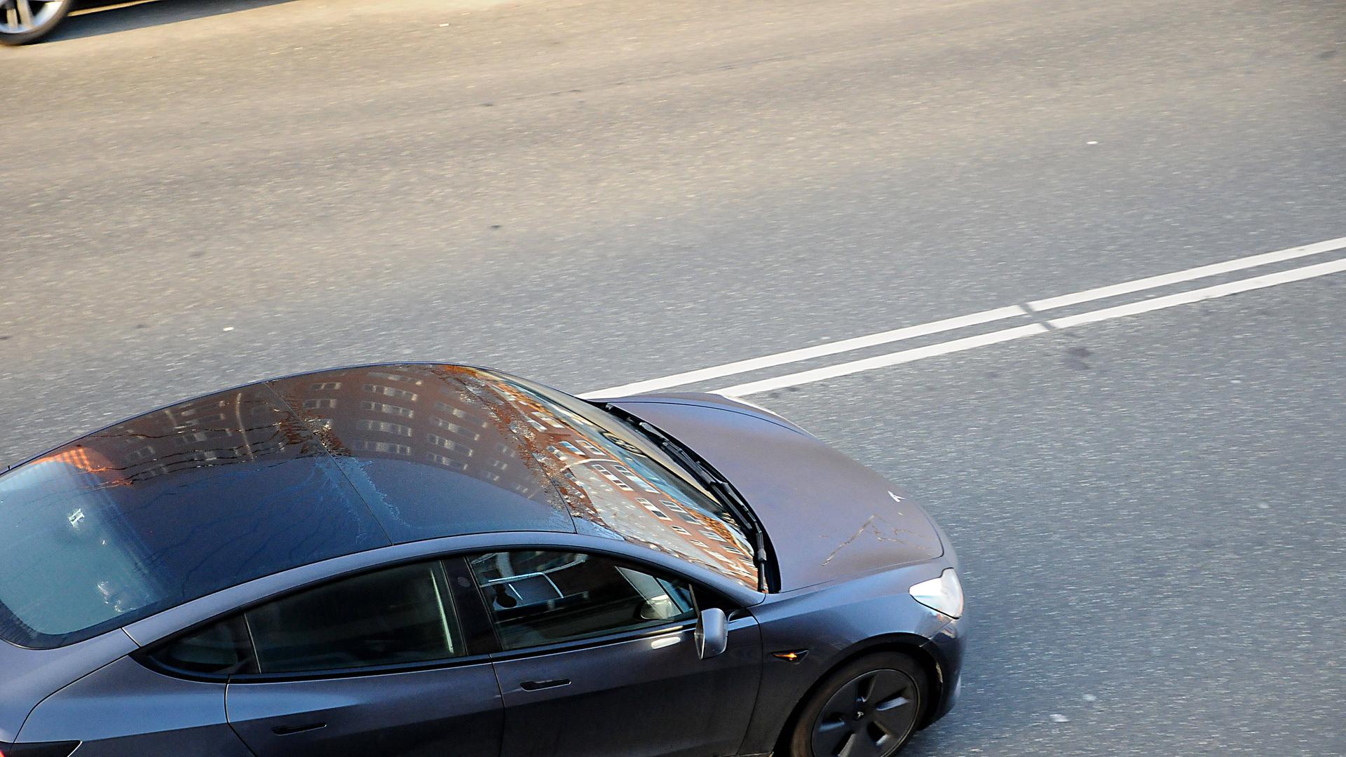 Ein schwarz-graues Auto der Marke Tesla fährt auf einer Straße. Das Bild zeigt das Auto von oben.