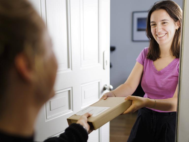 Eine Frau hat ihre Wohnungstür geöffnet. Sie reicht einer anderen Frau im Treppenhaus ein Paket entgegen. Eine Frau hat ihre Wohnungstür geöffnet. Sie reicht einer anderen Frau im Treppenhaus ein Paket entgegen.