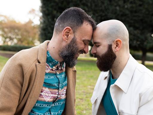 Zwei Männer lehnen ihre Köpfe liebevoll gegeneinander. Sie wirken vertraut.