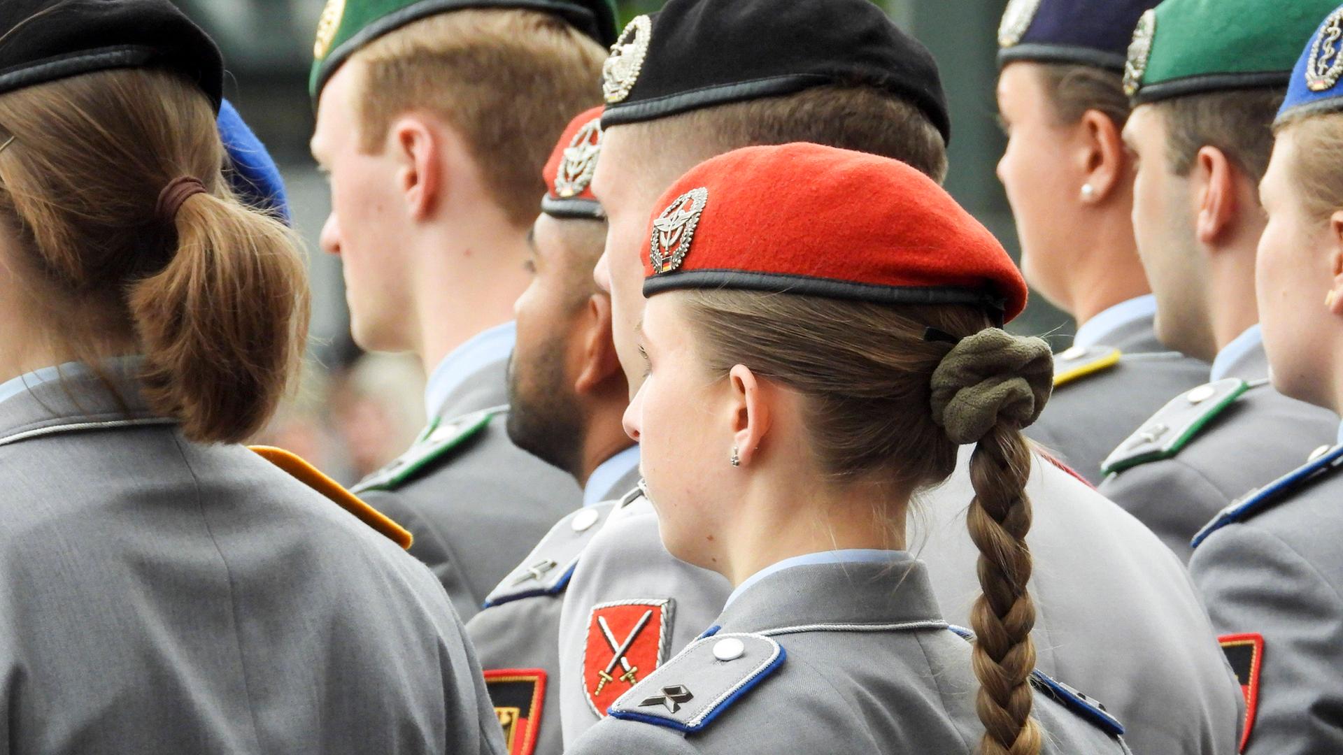 Soldaten und Soldatinnen in Uniform stehen nebeneinander, sie sind von hinten zu sehen. Eine Soldatin hat einen langen Zopf. Alle tragen Baretts. Aufnahme vom militärischen Appell bei der Parade zum Veteranentag am 15. Juni 2025.