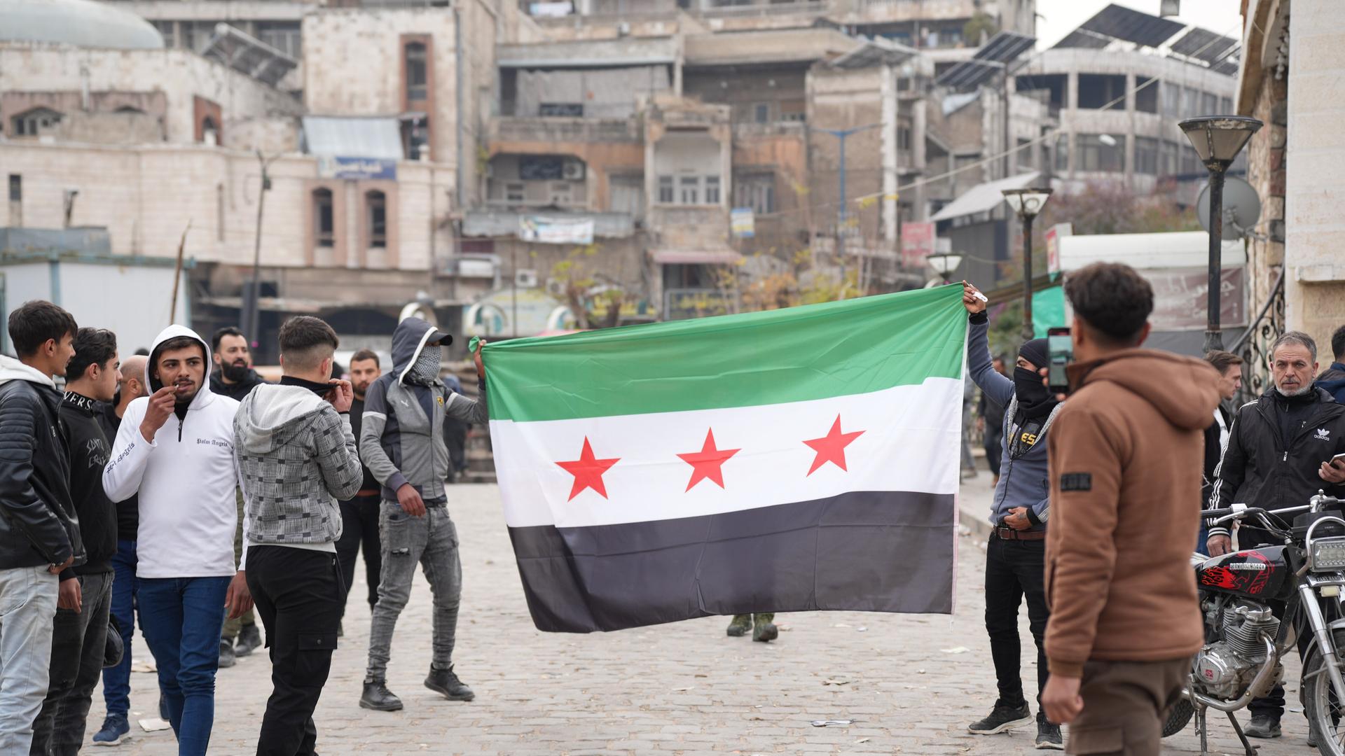 Junge Männer laufen mit aufgespannter syrischer Flagge durch die Stadt Hama