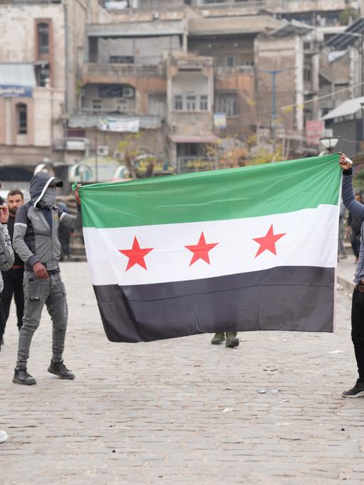 Junge Männer laufen mit aufgespannter syrischer Flagge durch die Stadt Hama Junge Männer laufen mit aufgespannter syrischer Flagge durch die Stadt Hama
