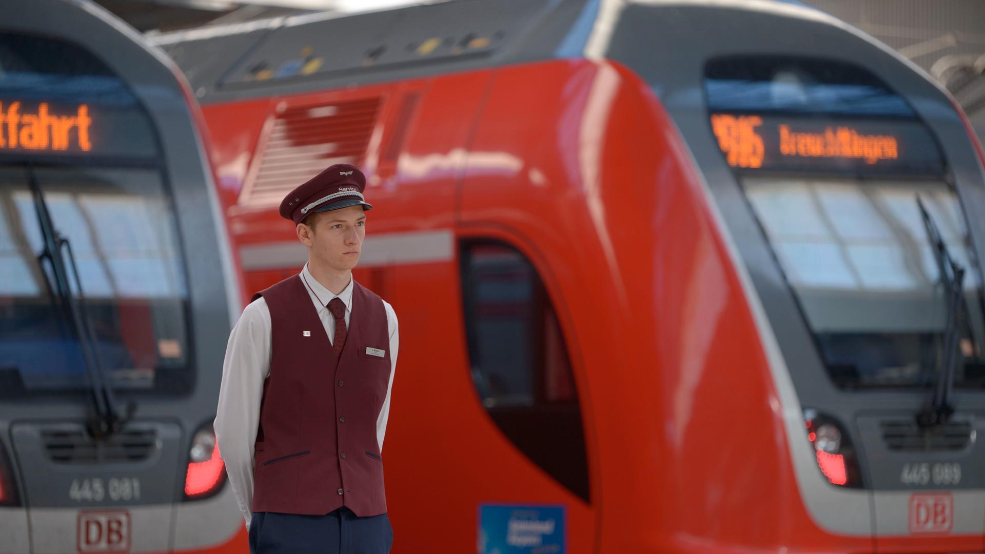 Ein Bahnmitarbeiter steht vor zwei Regionalzügen und schaut in die Ferne.