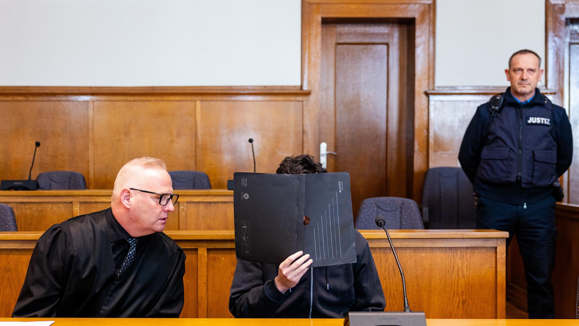 Ein Verteidiger sitzt neben seinem Mandanten in einem Saal des Landgerichts Saarbrücken. Der Angeklagte hat einen Polizisten mit einer Dienstwaffe erschossen.