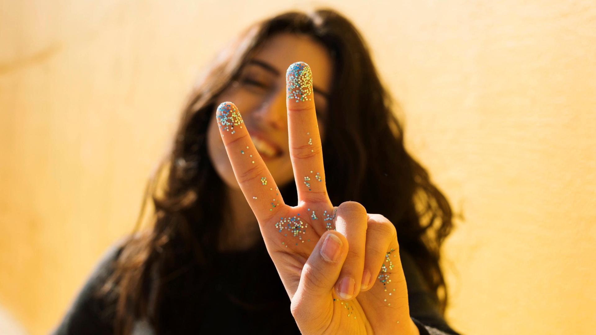 Eine Frau mit Glitzer an den Fingern macht ein Victory-Zeichen