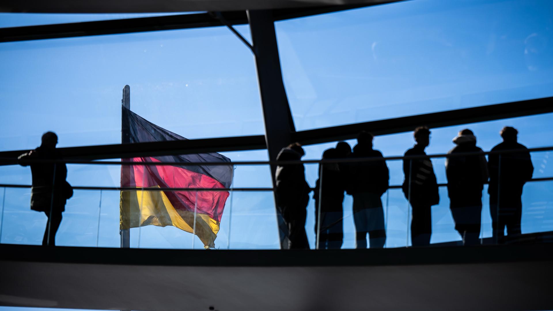 Besucher gehen vor der Deutschlandflagge in der Kuppel im Bundestag.