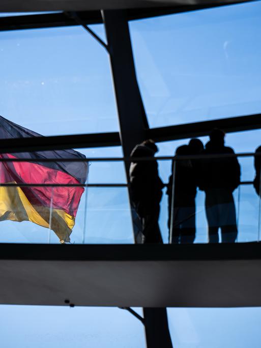 Besucher gehen vor der Deutschlandflagge in der Kuppel im Bundestag.