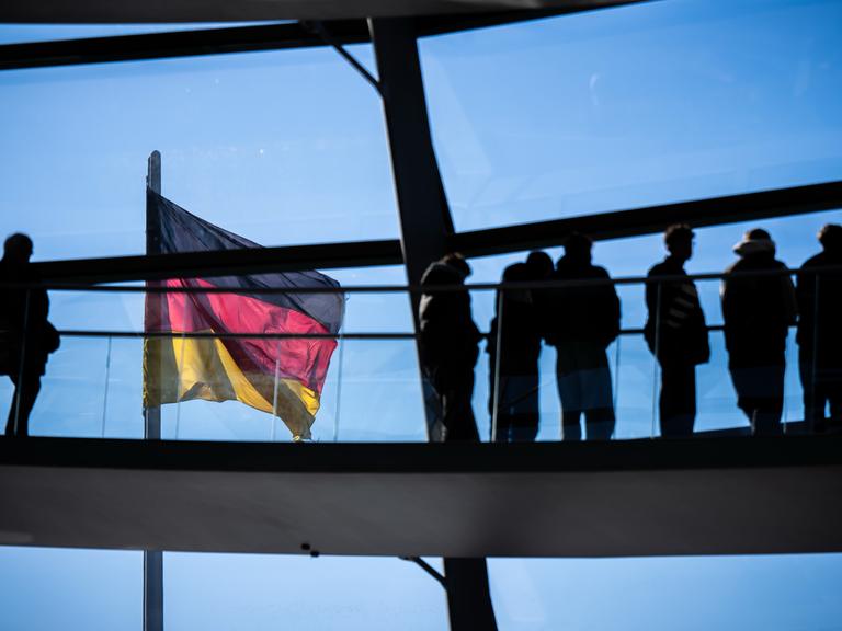 Besucher gehen vor der Deutschlandflagge in der Kuppel im Bundestag.