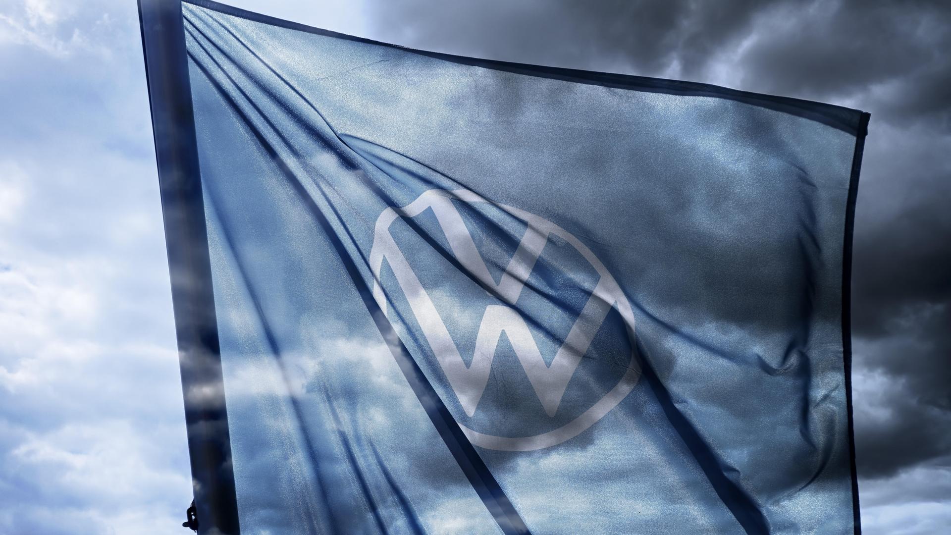 VW-Zeichen auf der Fahne, die vor dunklem Himmel weht.