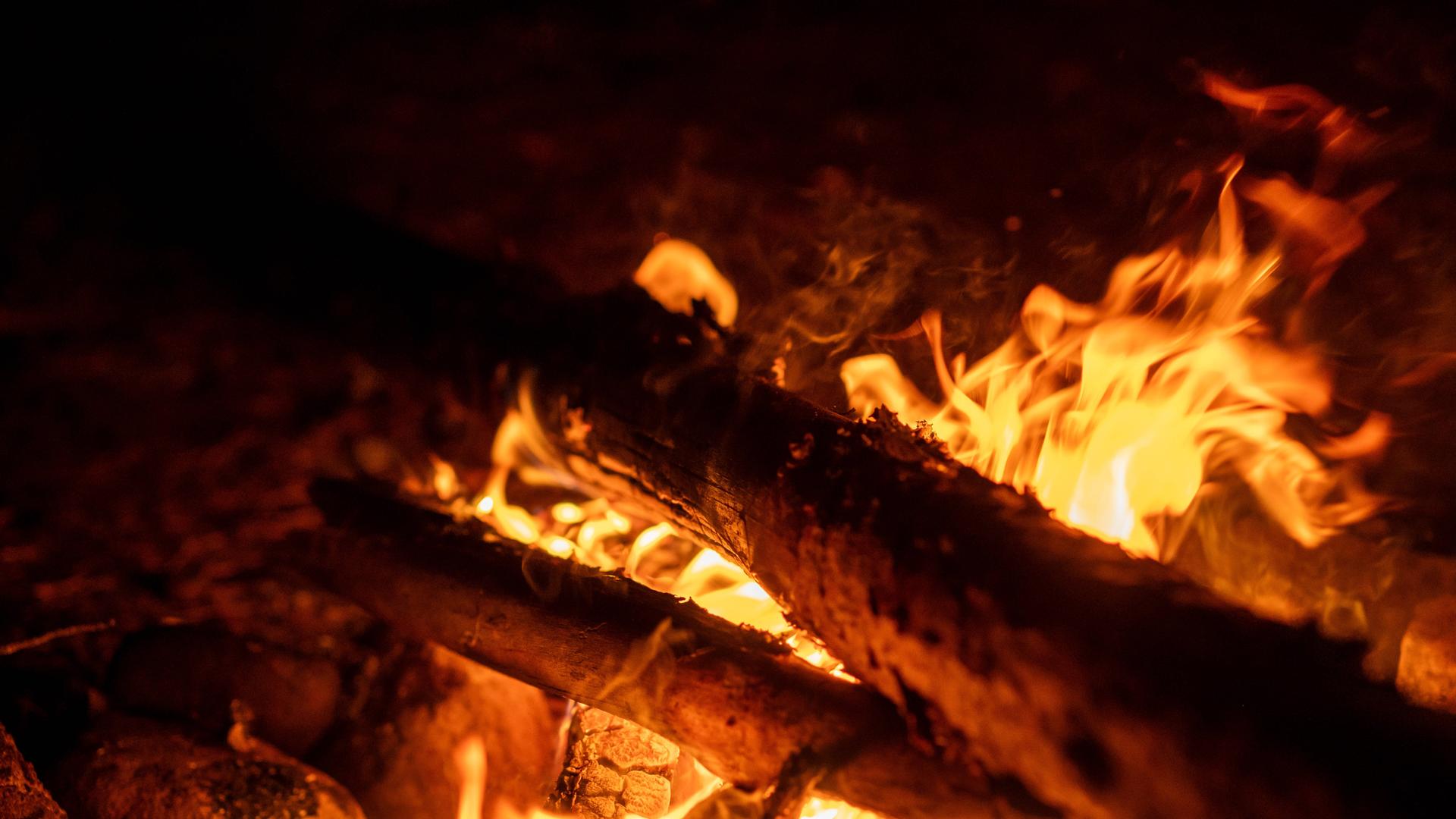 Nahaufnahme eines warm leuchtenden Lagerfeuers mit dicken, brennenden Ästen im Dunkeln Nahaufnahme eines warm leuchtenden Lagerfeuers mit dicken, brennenden Ästen im Dunkeln