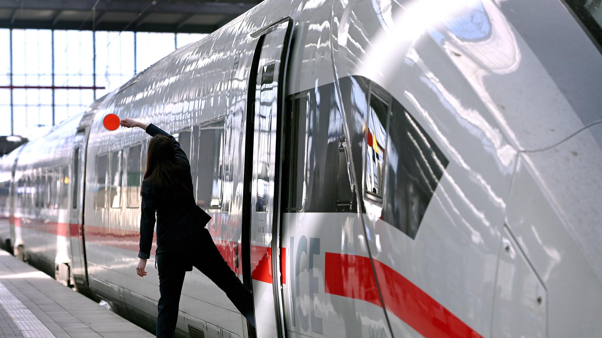 Zugbegleiterin signalisiert dem Lokfuehrer mit roter Kelle, dass der ICE zur Abfahrt bereit ist.