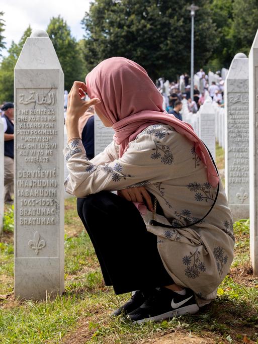 Eine Frau kniet am Mahnmal von Srebrenica