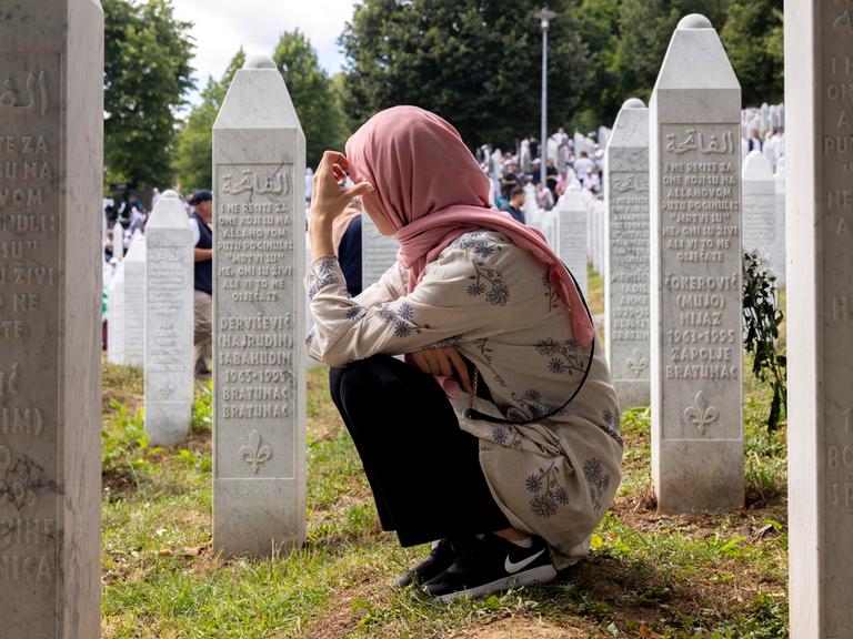 Eine Frau kniet am Mahnmal von Srebrenica