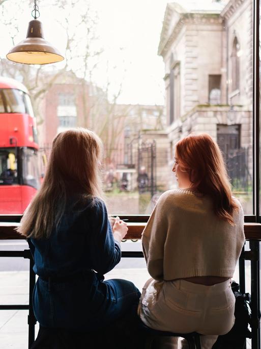 Zwei Frauen sitzen in einem Café nebeneinander Zwei Frauen sitzen in einem Café nebeneinander