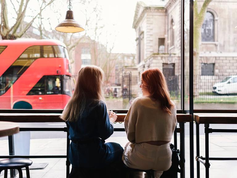 Zwei Frauen sitzen in einem Café nebeneinander Zwei Frauen sitzen in einem Café nebeneinander