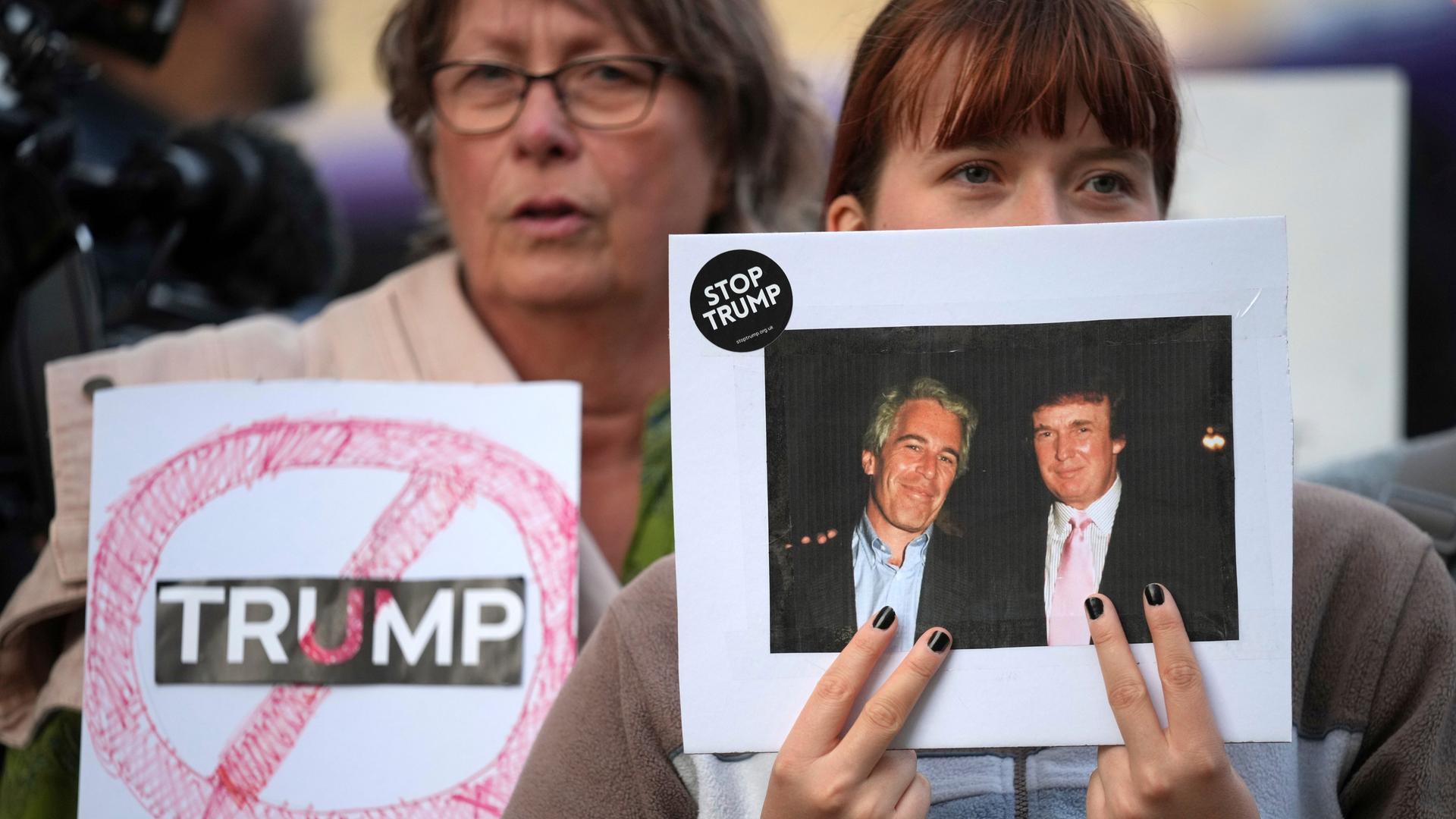 Bei einem Anti-Trump-Protest hält eine Frau ein altes Foto hoch, das Donald Trump und Jeffrey Epstein zusammen zeigt. Am Rand des Bildes klebt ein Sticker mit der Aufschrift "Stop Trump". Bei einem Anti-Trump-Protest hält eine Frau ein altes Foto hoch, das Donald Trump und Jeffrey Epstein zusammen zeigt. Am Rand des Bildes klebt ein Sticker mit der Aufschrift "Stop Trump".