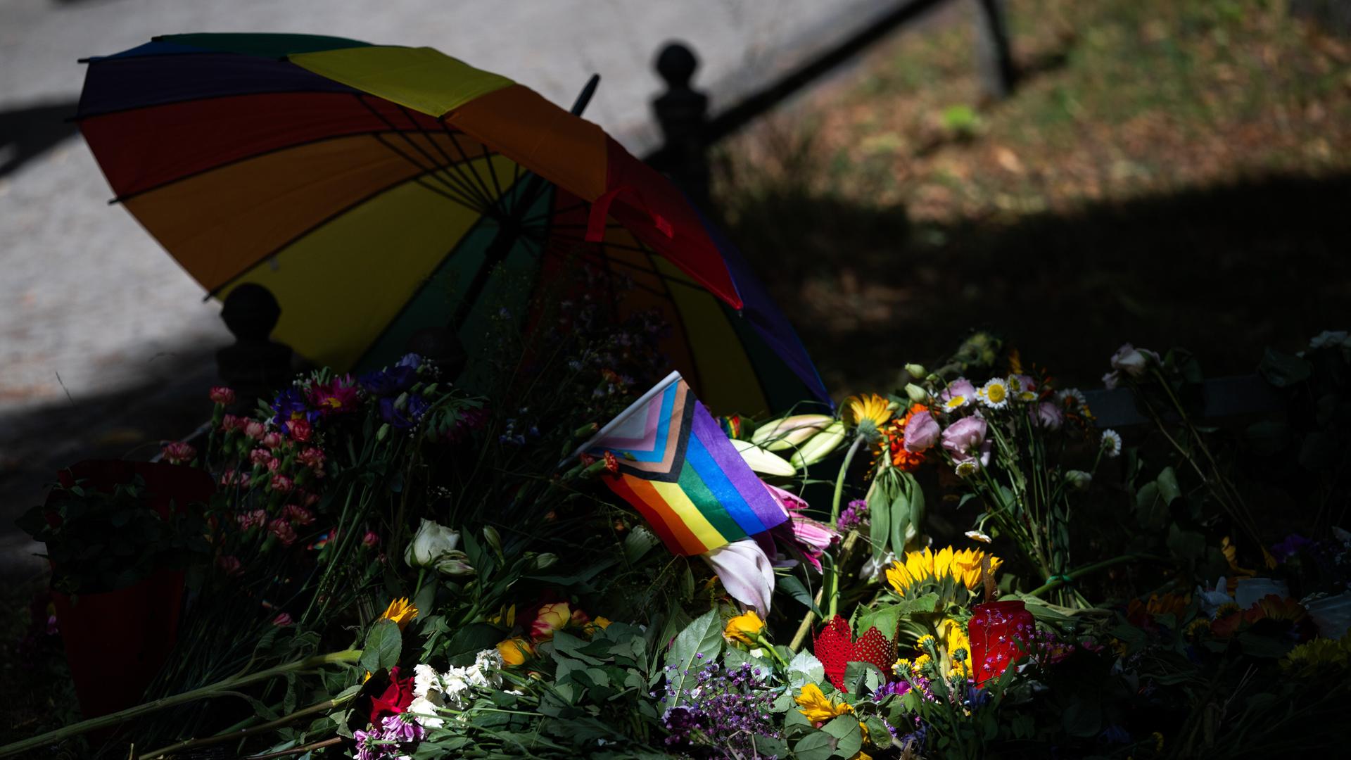 Die Sonne scheint auf Blumen und eine Progress-Pride-Fahne, die zum Gedenken an die Opfer des Anschlags auf den CSD abgelegt wurden.