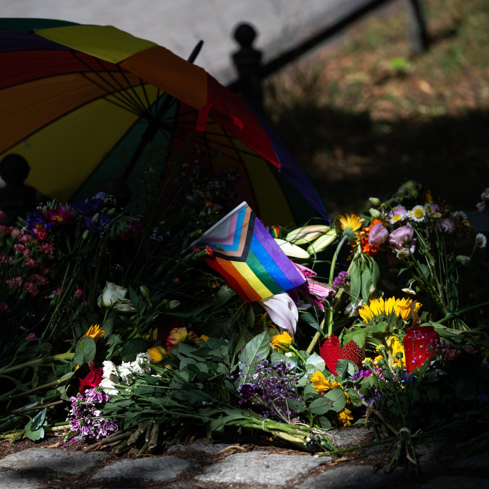 Die Sonne scheint auf Blumen und eine Progress-Pride-Fahne, die zum Gedenken an die Opfer des Anschlags auf den CSD abgelegt wurden.