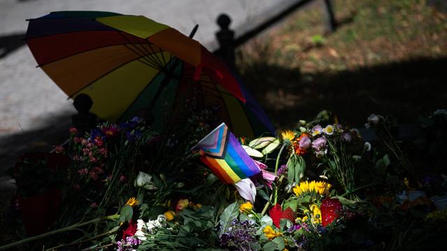 Die Sonne scheint auf Blumen und eine Progress-Pride-Fahne, die zum Gedenken an die Opfer des Anschlags auf den CSD abgelegt wurden.