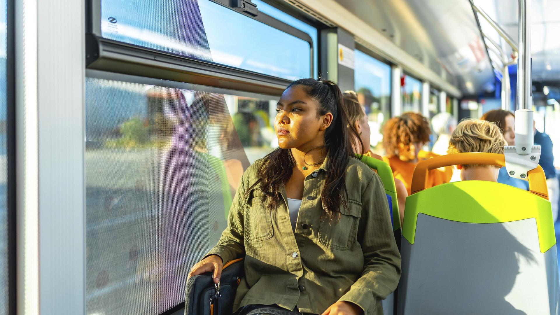 Eine junge Frau sitzt am Fenster eines öffentlichen Verkehrsbusses und schaut nachdenklich nach draußen Eine junge Frau sitzt am Fenster eines öffentlichen Verkehrsbusses und schaut nachdenklich nach draußen