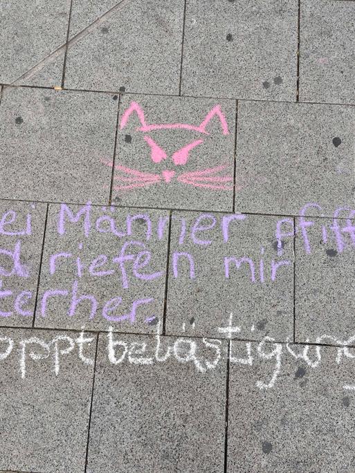 "Zwei Männer pfiffen und riefen mir hinterher - #stoppbelästigung" steht mit Kreide geschrieben auf einer Straße