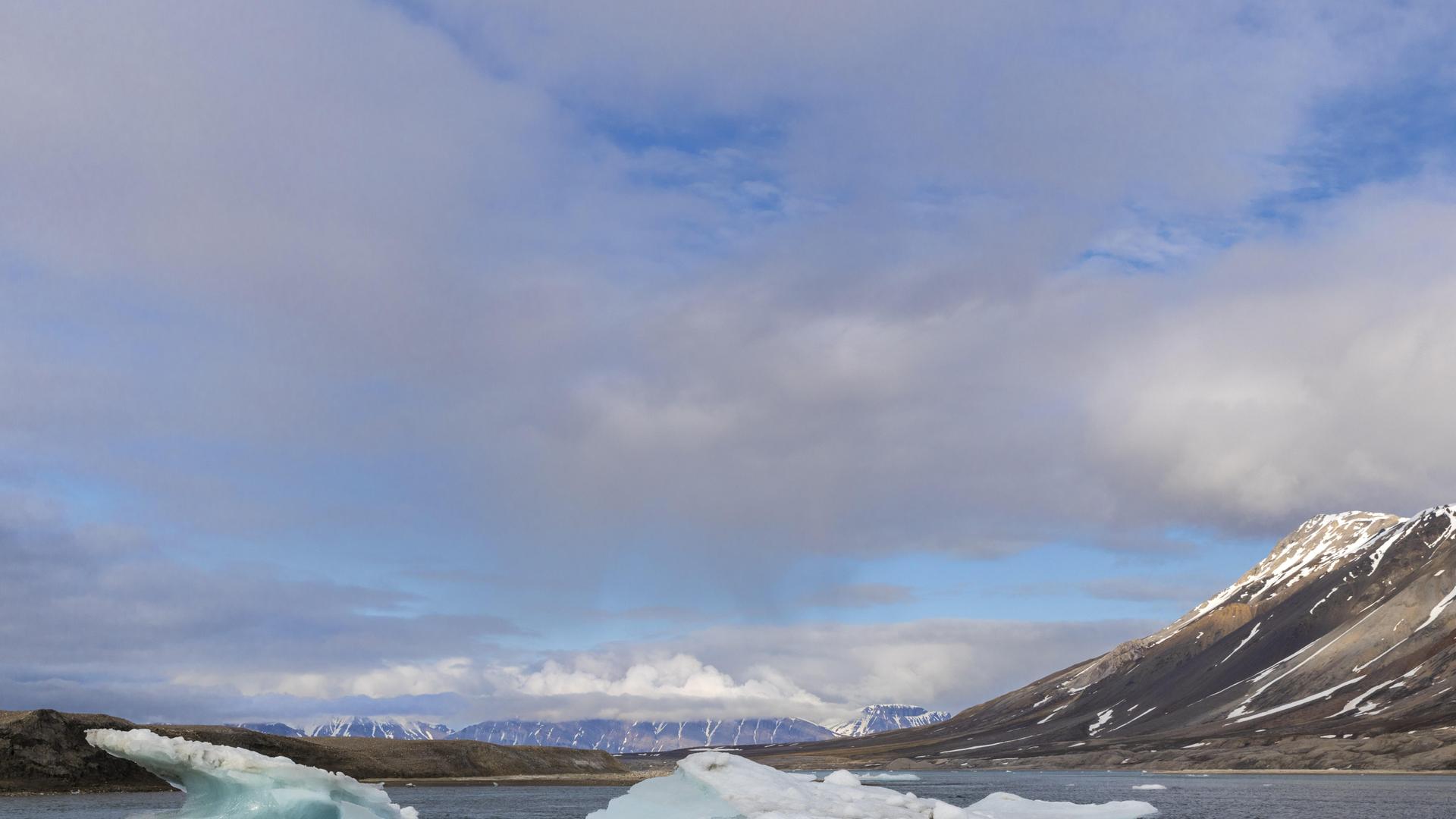 Eine Eisscholle treibt im Meer in der Bucht vor dem Gletscher Recherchebreen bei Spitzbergen, Svalbard. Der Himmel ist bewölkt bis heiter. Die Berge im Hintergrund sind nur wenig mit Schnee bedeckt. Eine Eisscholle treibt im Meer in der Bucht vor dem Gletscher Recherchebreen bei Spitzbergen, Svalbard. Der Himmel ist bewölkt bis heiter. Die Berge im Hintergrund sind nur wenig mit Schnee bedeckt.