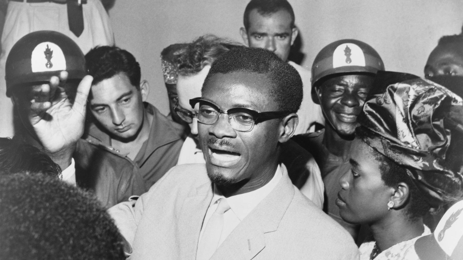 Schwarz-weiß-Foto: Im Oktober 1960 steht Kongos Premierminister Patrice Lumumba in einer Menschentraube und spricht zu seinen Anhängern. Er trägt eine Brille und Anzug. Schwarz-weiß-Foto: Im Oktober 1960 steht Kongos Premierminister Patrice Lumumba in einer Menschentraube und spricht zu seinen Anhängern. Er trägt eine Brille und Anzug.
