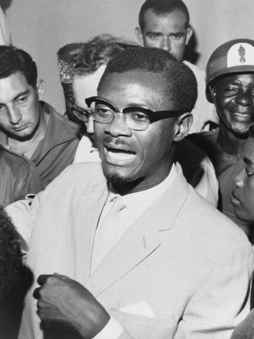 Schwarz-weiß-Foto: Im Oktober 1960 steht Kongos Premierminister Patrice Lumumba in einer Menschentraube und spricht zu seinen Anhängern. Er trägt eine Brille und Anzug.