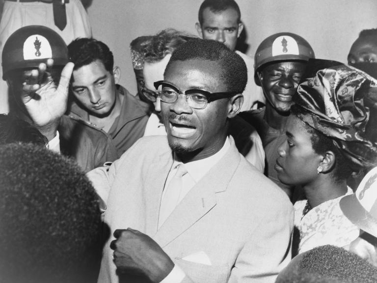 Schwarz-weiß-Foto: Im Oktober 1960 steht Kongos Premierminister Patrice Lumumba in einer Menschentraube und spricht zu seinen Anhängern. Er trägt eine Brille und Anzug.