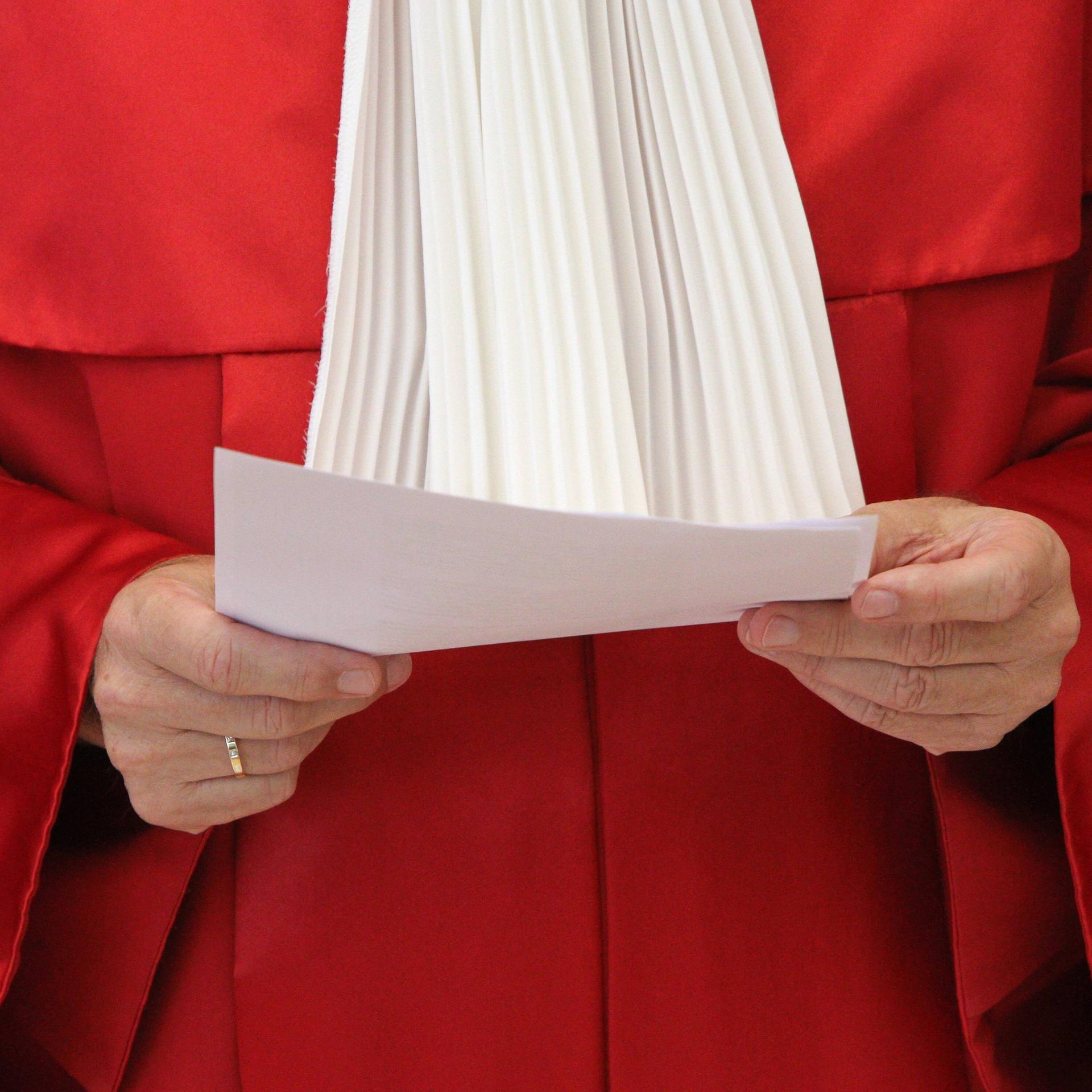 Die rote Robe eines Richters des Bundesverfassungsgericht. Die Person hält ein Papier in der Hand. Kopf und Beine sind nicht zu sehen.