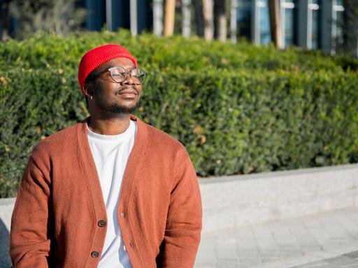 Mann mit roter Mütze und Strickjacke hält Gesicht in die Sonne