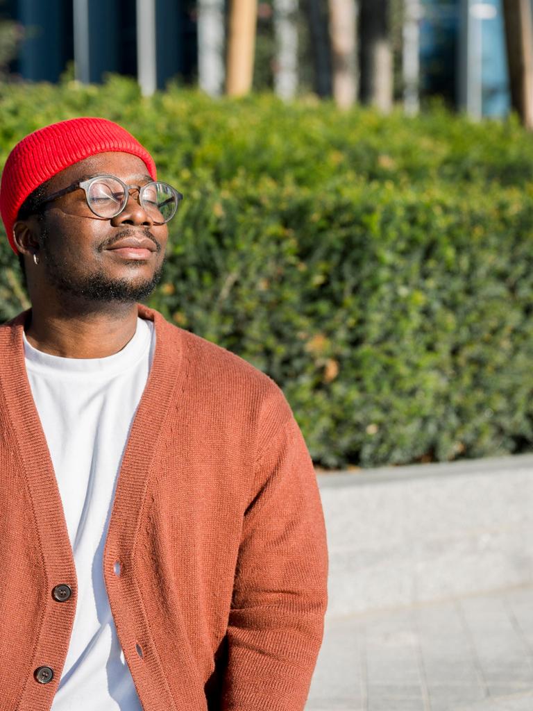 Mann mit roter Mütze und Strickjacke hält Gesicht in die Sonne