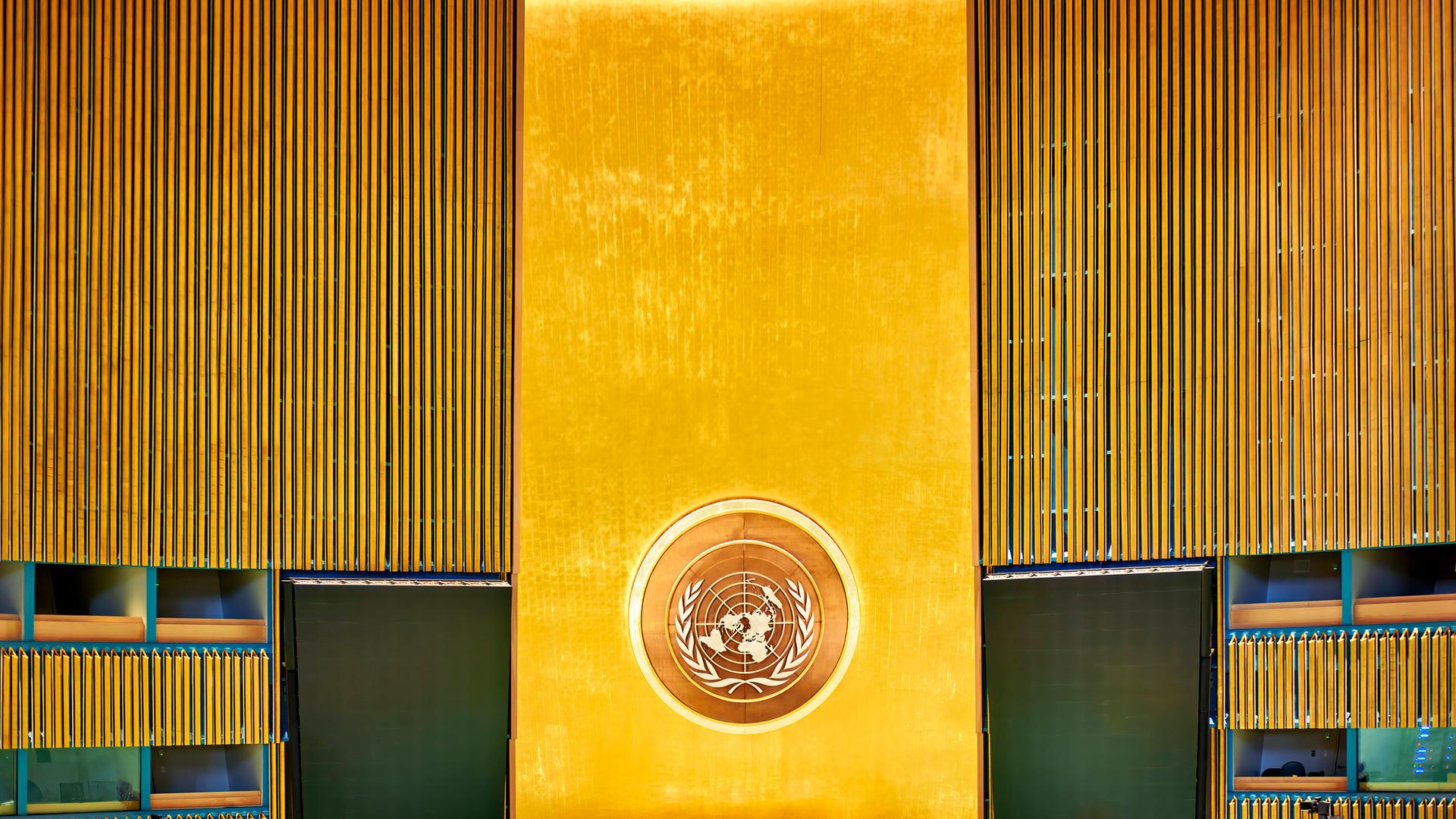 Leerer Plenarsaal der Vereinten Nationen in New York City. Blick auf das Rednerpult, die Wand dahinter ist golden.