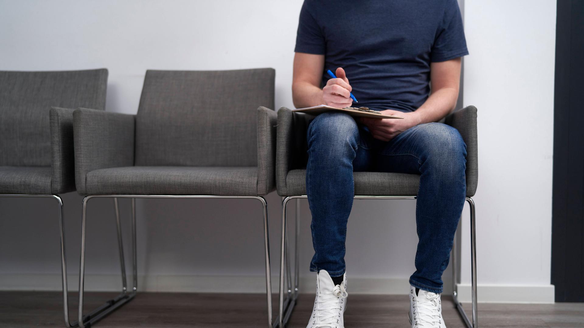 Ein Mann sitzt im Wartezimmer und füllt einen Fragebogen aus. Ein Mann sitzt im Wartezimmer und füllt einen Fragebogen aus.