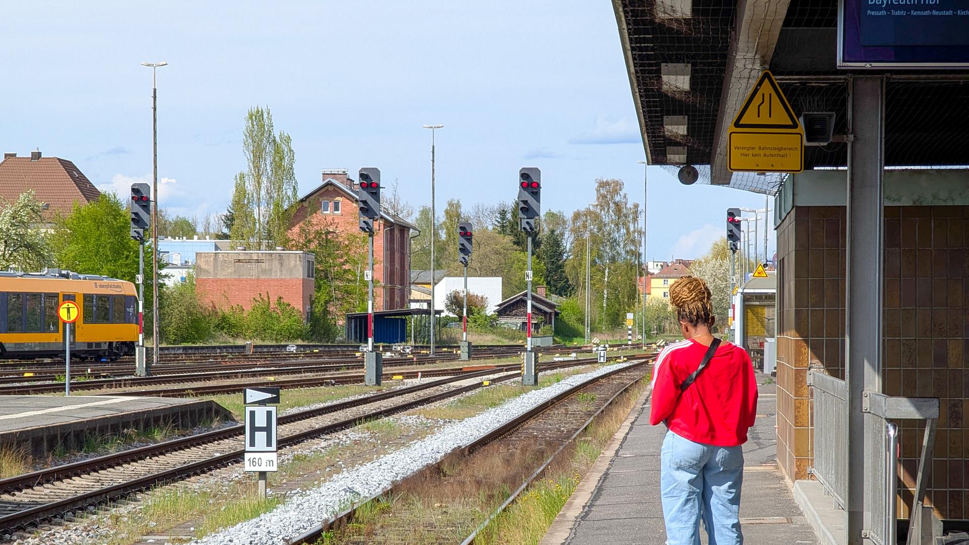Eine Frau steht auf dem Bahnsteig und ihre Tasche steht auf den Boden, während sie am Bahnhof Weiden in Bayern auf einen Zug wartet. Eine Frau steht auf dem Bahnsteig und ihre Tasche steht auf den Boden, während sie am Bahnhof Weiden in Bayern auf einen Zug wartet.