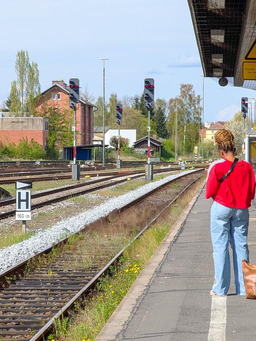 Eine Frau steht auf dem Bahnsteig und ihre Tasche steht auf den Boden, während sie am Bahnhof Weiden in Bayern auf einen Zug wartet. Eine Frau steht auf dem Bahnsteig und ihre Tasche steht auf den Boden, während sie am Bahnhof Weiden in Bayern auf einen Zug wartet.
